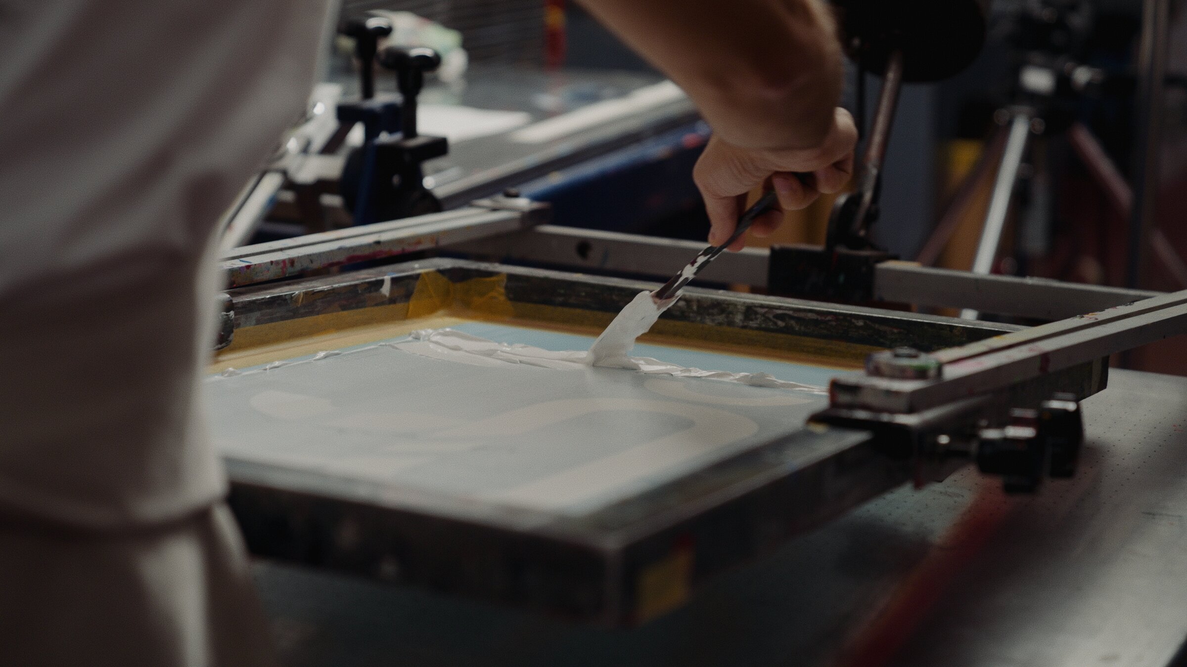 Applying white ink with a squeegee across a screen-printing frame