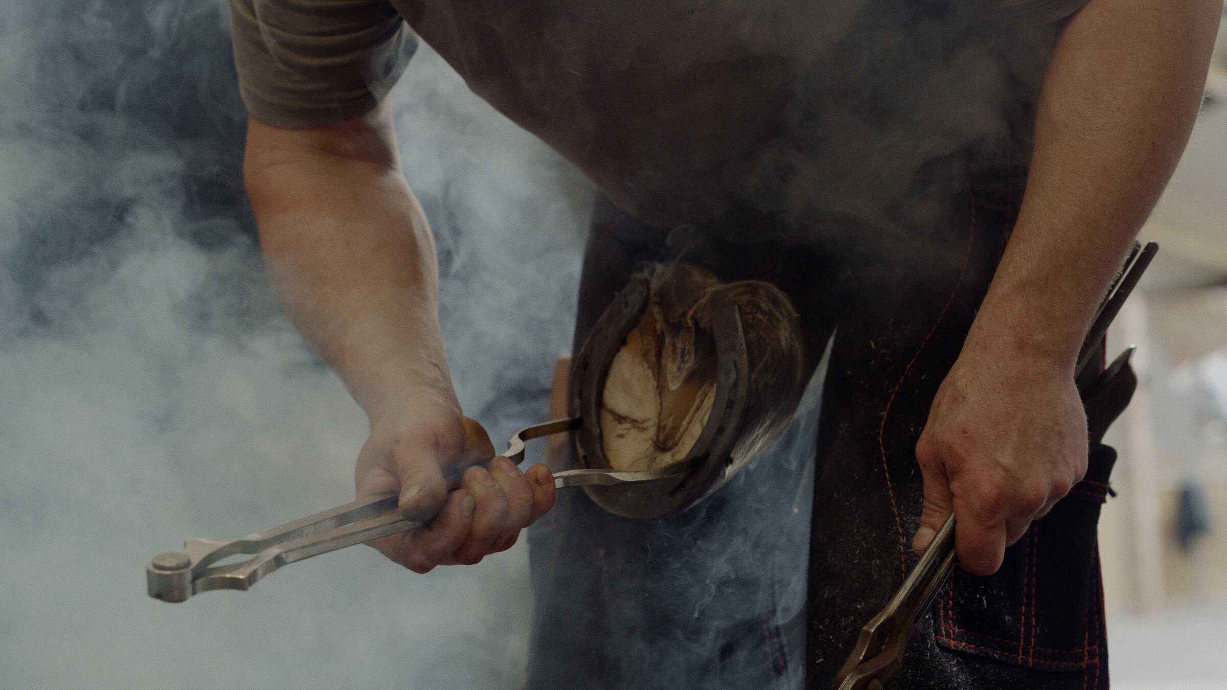 Farrier shoeing a horse in a cloud of hot-fit smoke