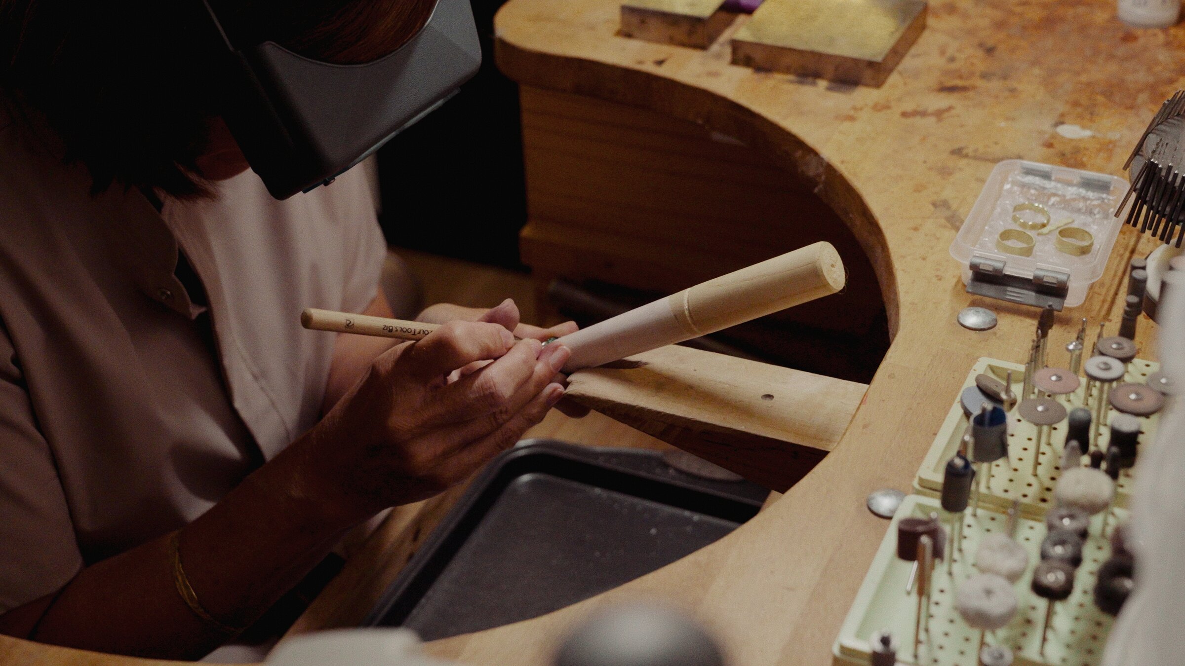 Jeweller shaping a ring on a wooden mandrel, rings laid out nearby