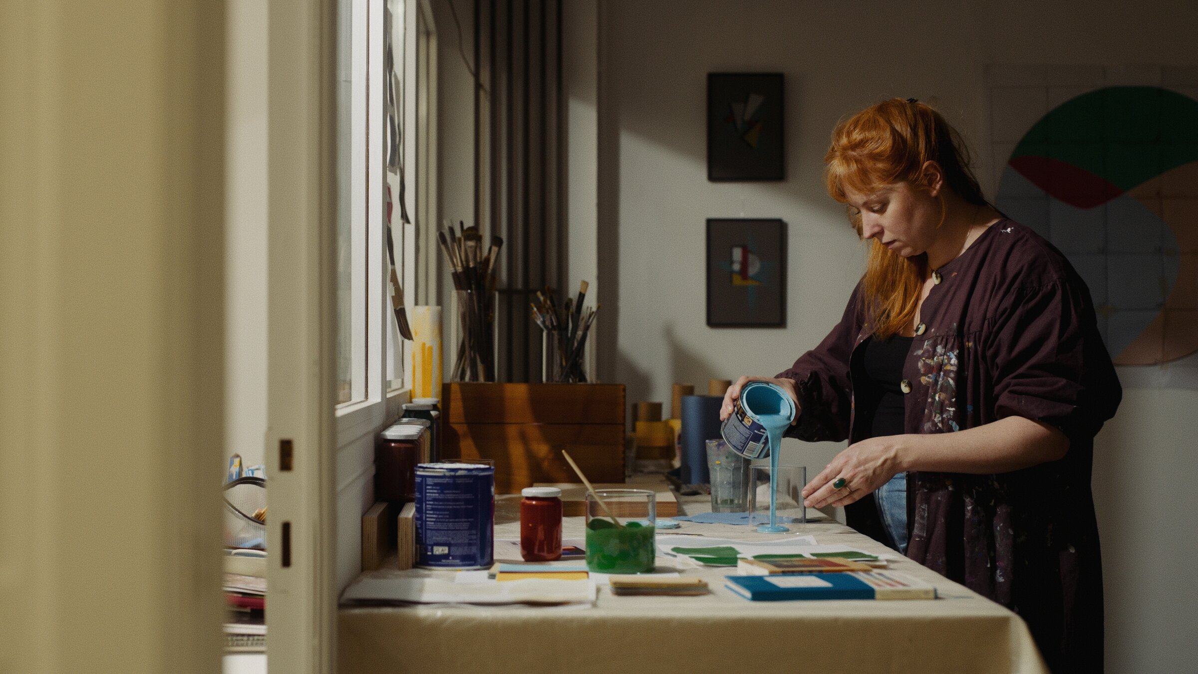 Painter mixing blue paint in her studio, pouring from a can into a glass