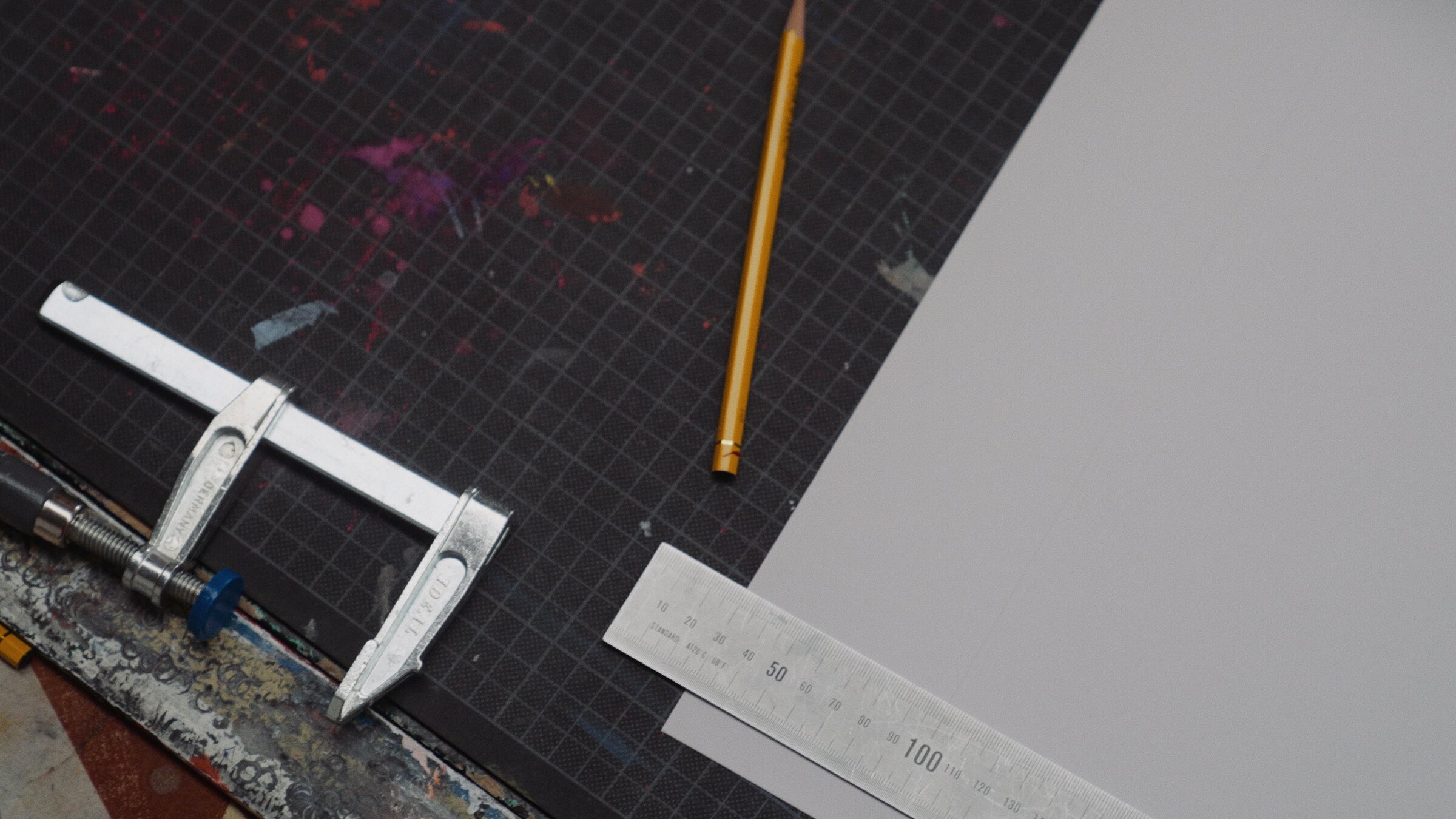 Screen-printing workbench detail, clamp and ruler on an ink-stained mat