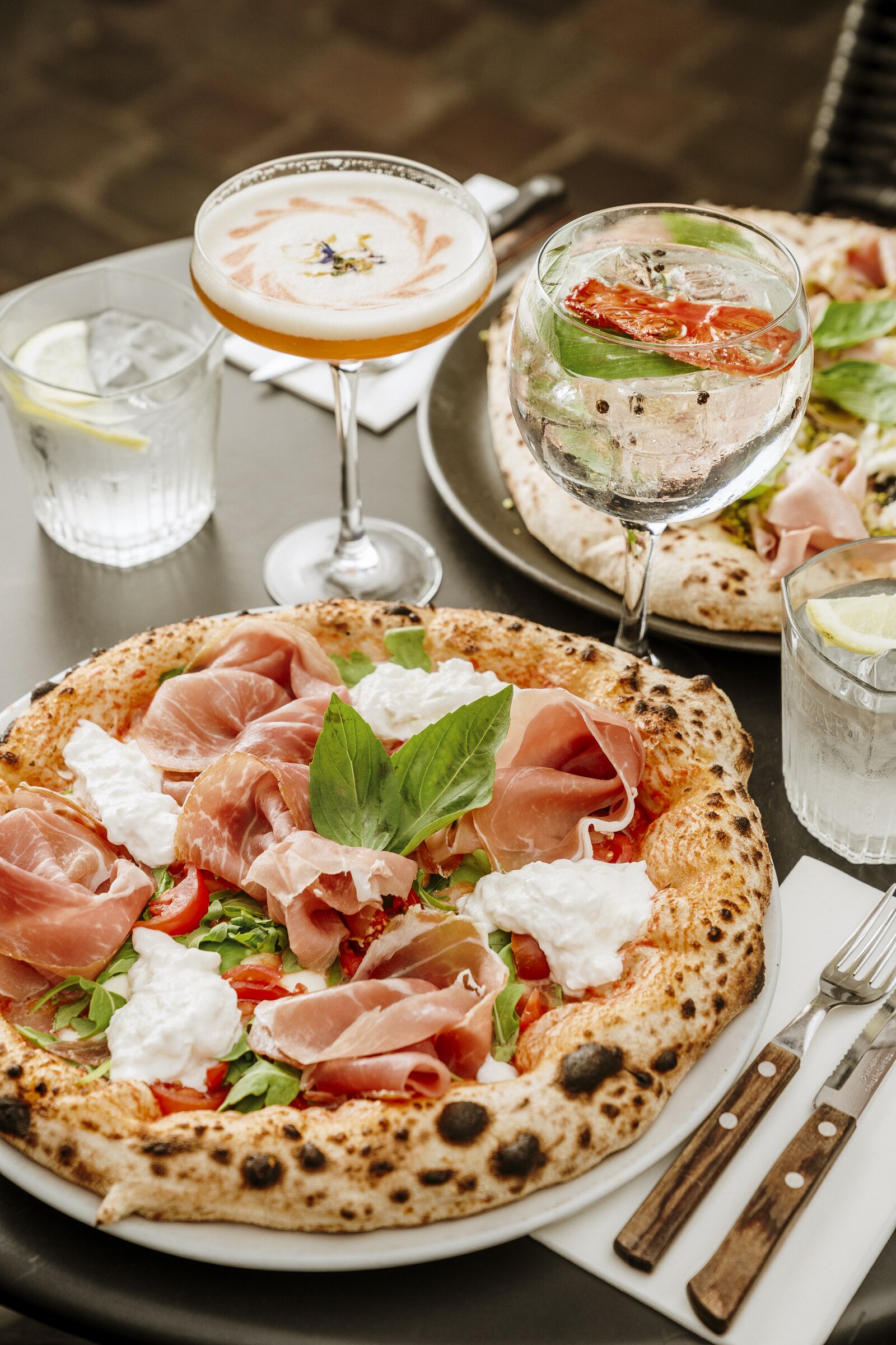 Neapolitan pizza with prosciutto and burrata, cocktails on a restaurant table