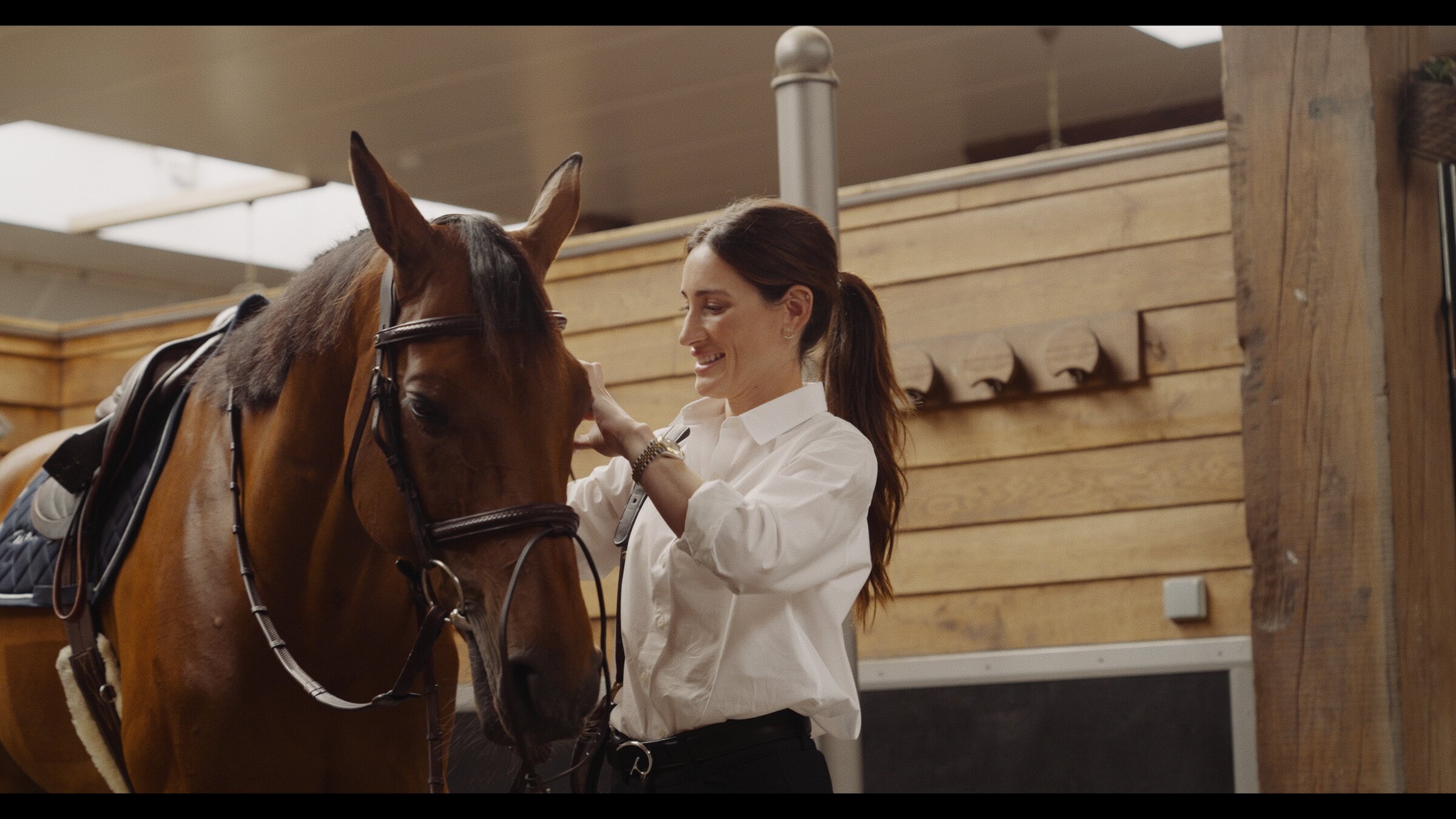 Rider petting her horse's face in the stable, smiling
