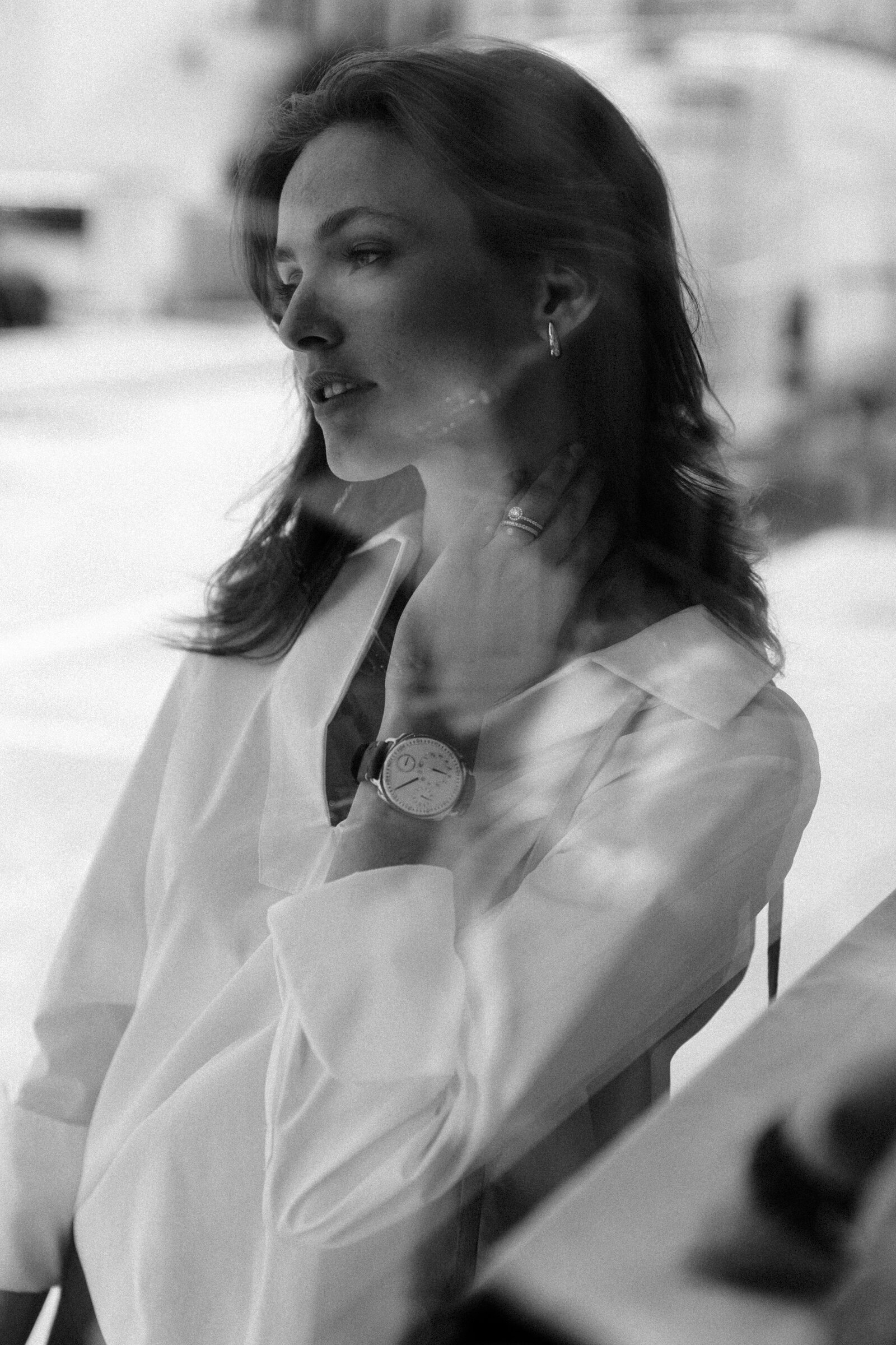 Black-and-white profile portrait, hand at neck, round watch and diamond rings