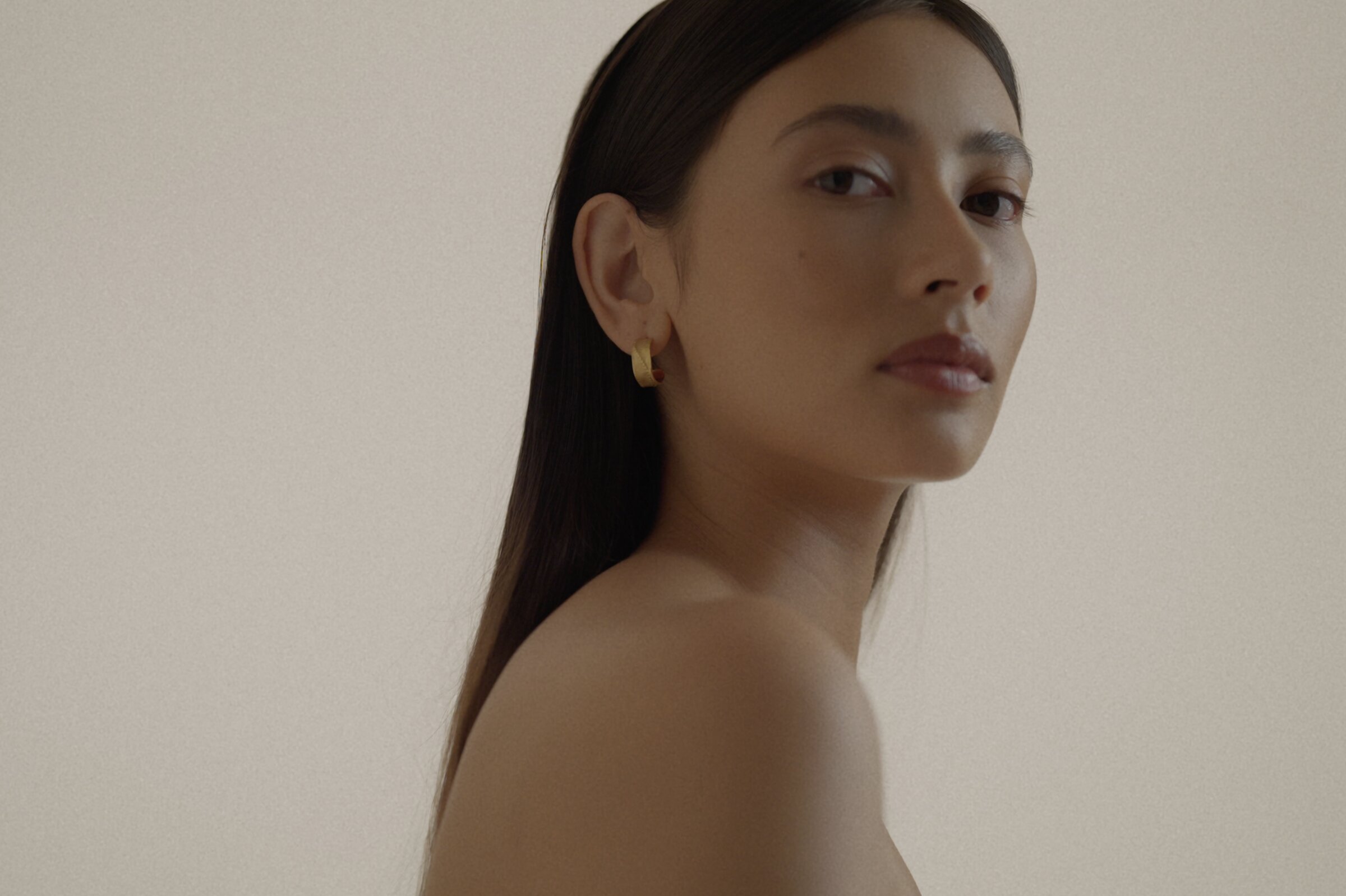 Model portrait wearing a gold earring, bare shoulder, minimal backdrop