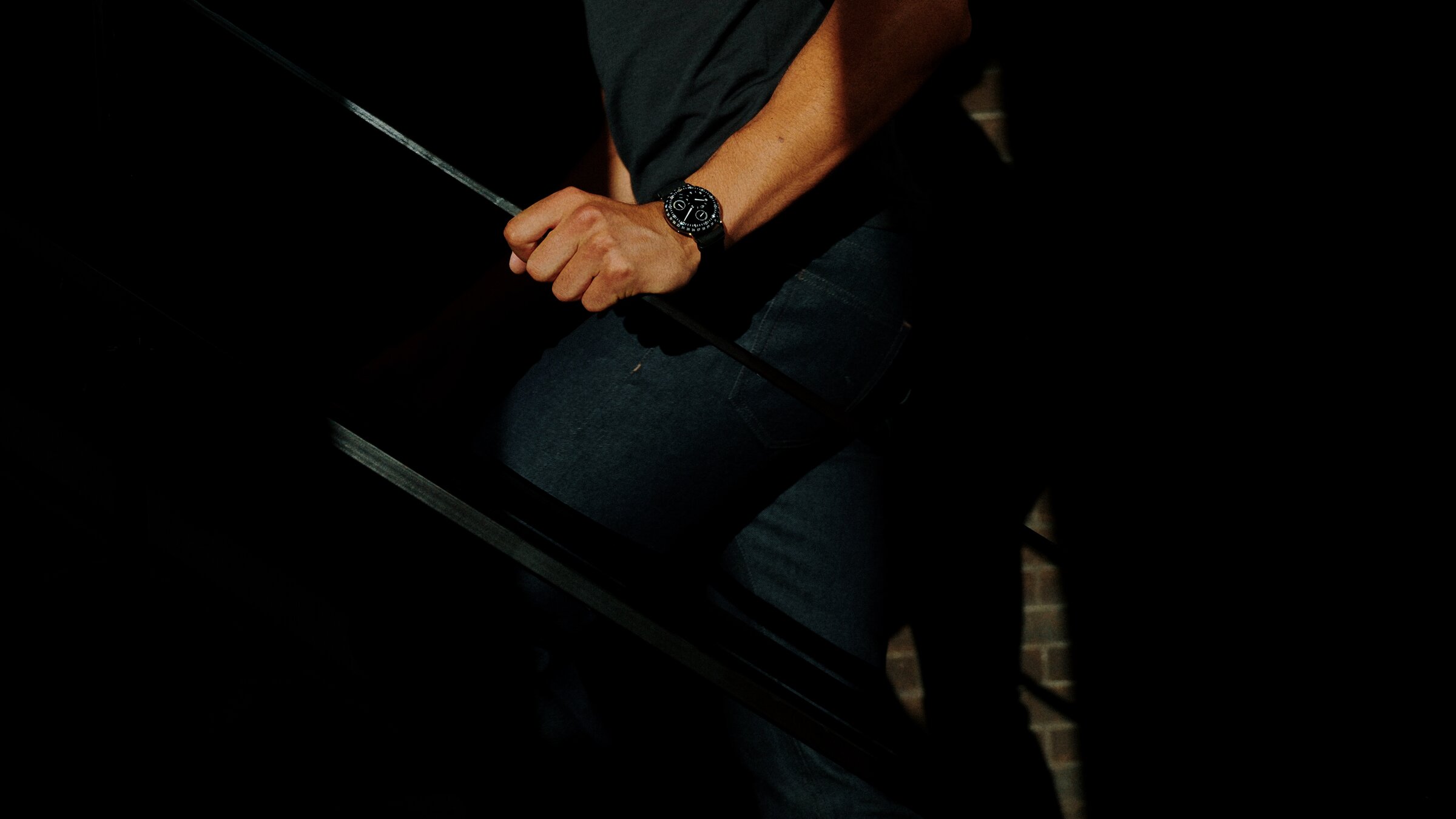Ressence black watch on wrist, descending a staircase in dramatic side light